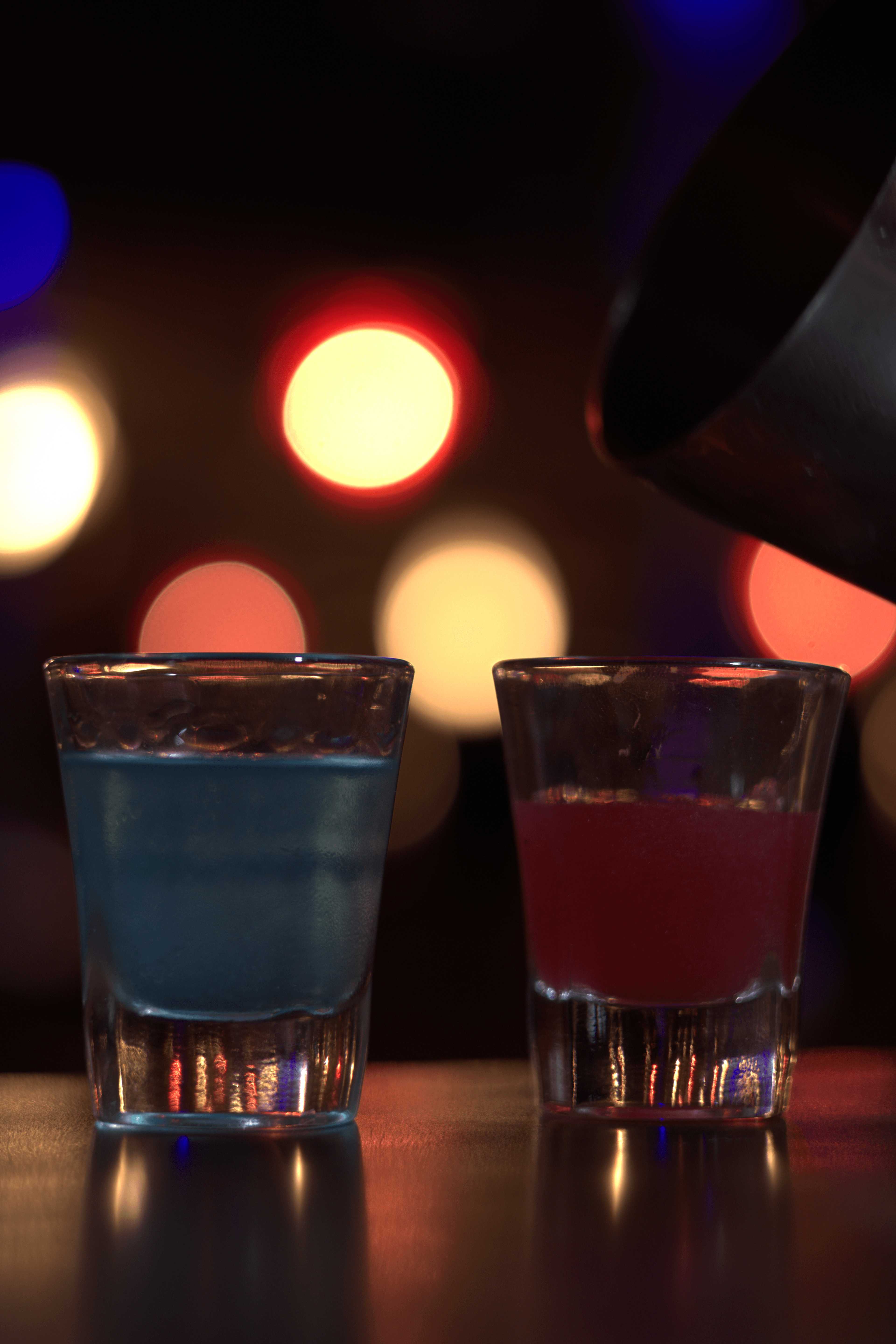 Blue and pink shot glasses on a bar with moody background lights