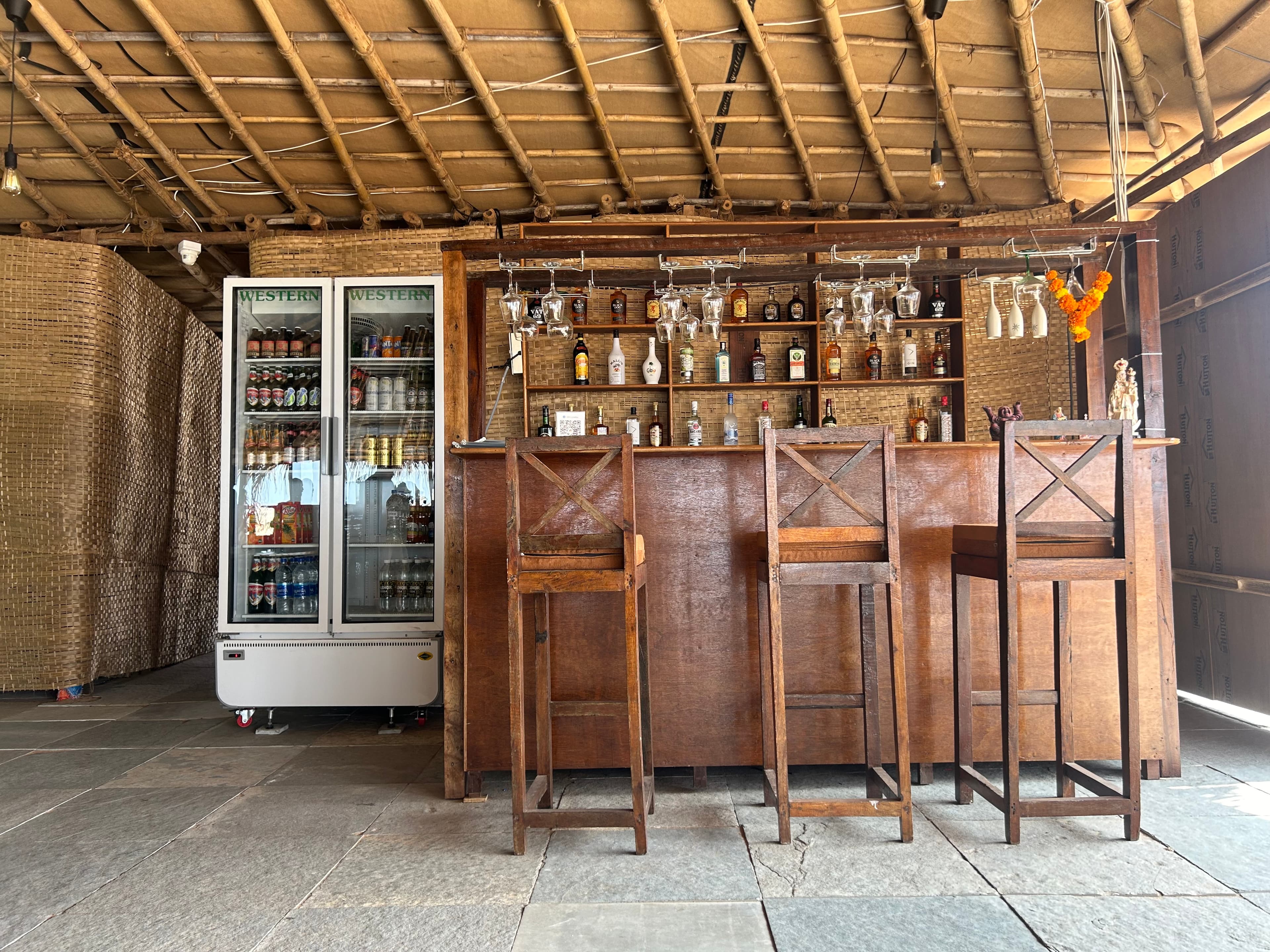 Rustic wooden bar with stools, spirits, and a stocked drinks refrigerator