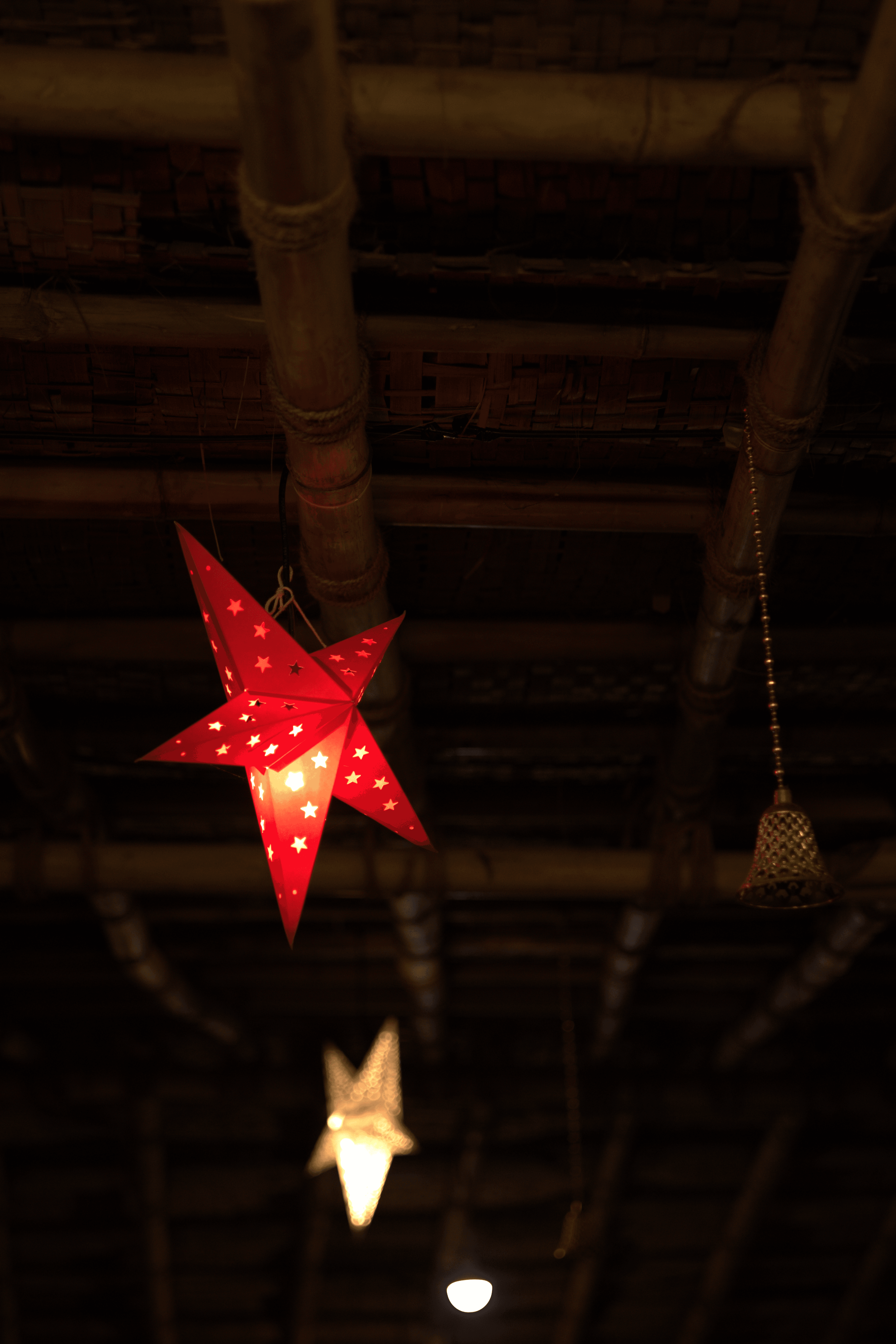 Illuminated red star lantern hanging from a bamboo and thatch ceiling